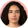 A woman with long, curly black hair and medium skin tone looks directly at the camera with a neutral expression. The background is pink and circular.