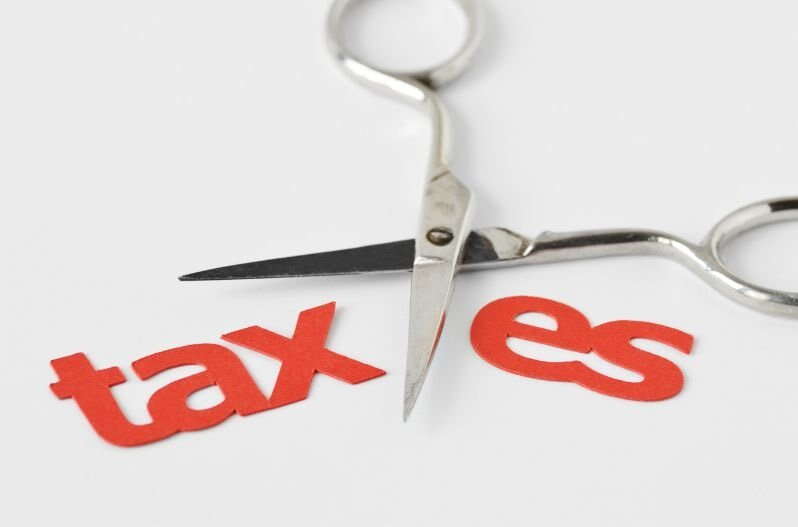 A pair of scissors cutting through the word "taxes," separating "tax" and "es," symbolizing a tax free business sale or tax cuts.