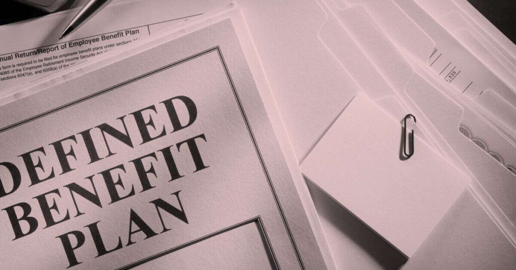 A close-up of documents on a desk, with "DEFINED BENEFIT PLAN" in large print, folders, a paper clip, blank note cards, and part of an employee benefit plan report—perfect for comparing defined benefit plan vs cash balance plan options.